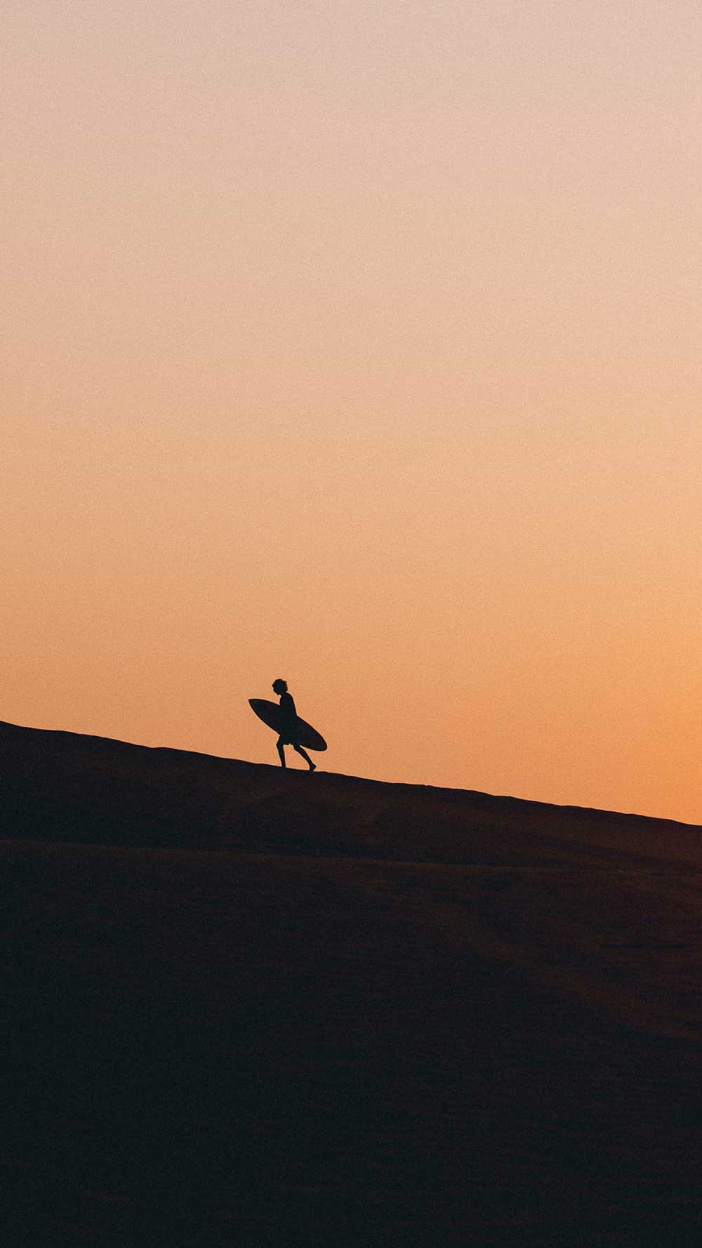 Silhouette of a person with a surfboard against an orange sunset sky.