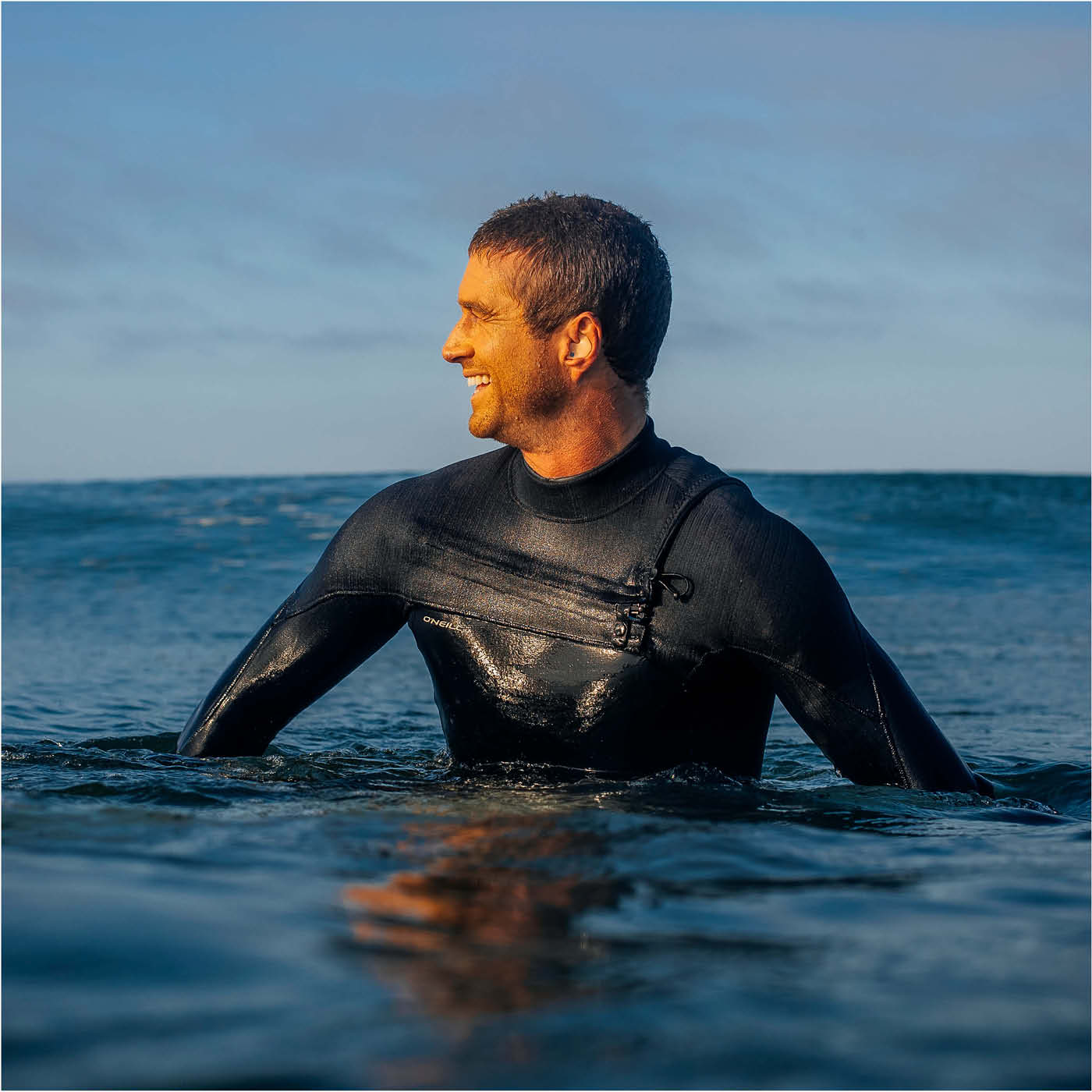 Man in a wetsuit standing in the ocean with a blue sky background