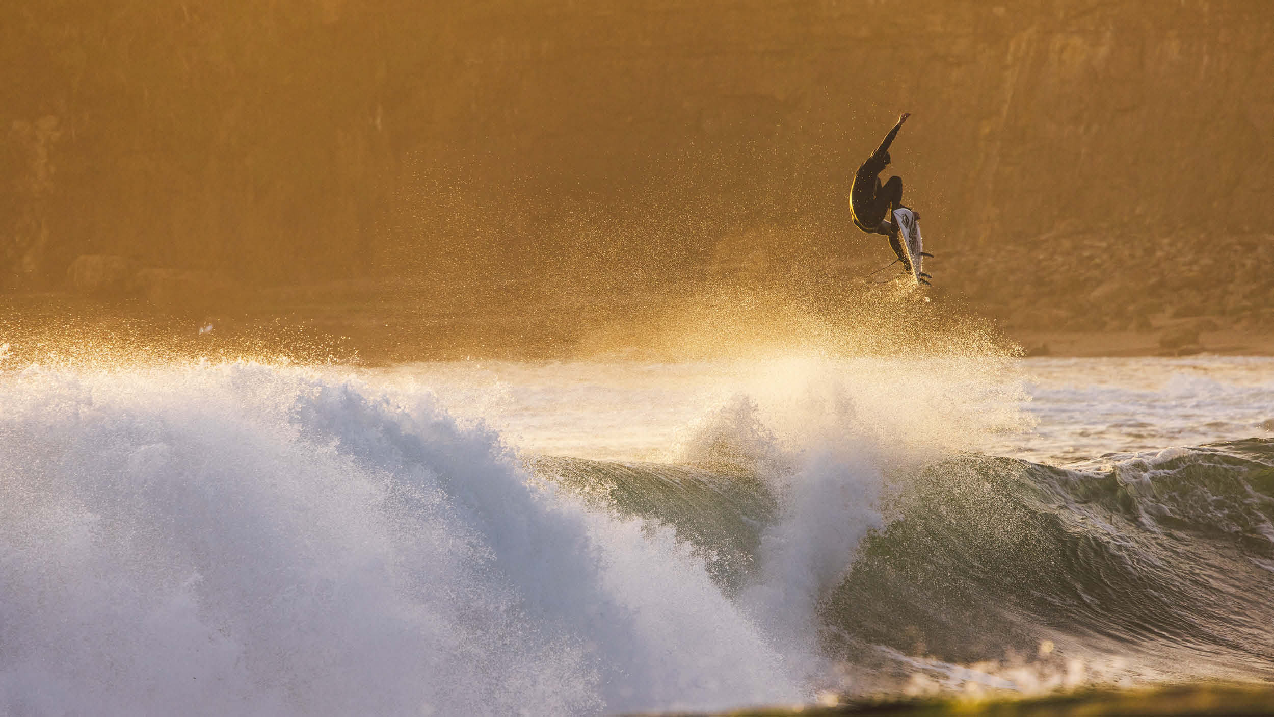 Surfer in mid-air above a wave with a golden sunset background