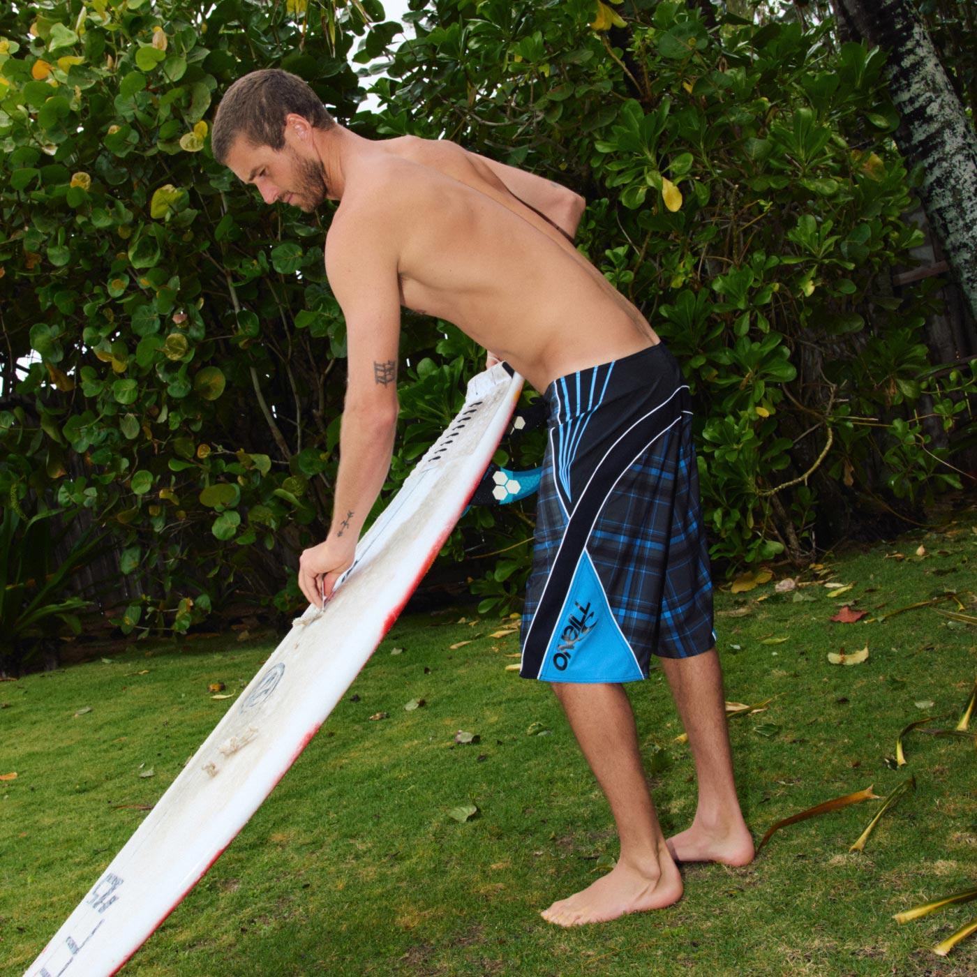 Man holding a surfboard on grass with greenery in the background