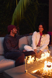 Two people sitting on a couch by a fire pit with palm trees in the background