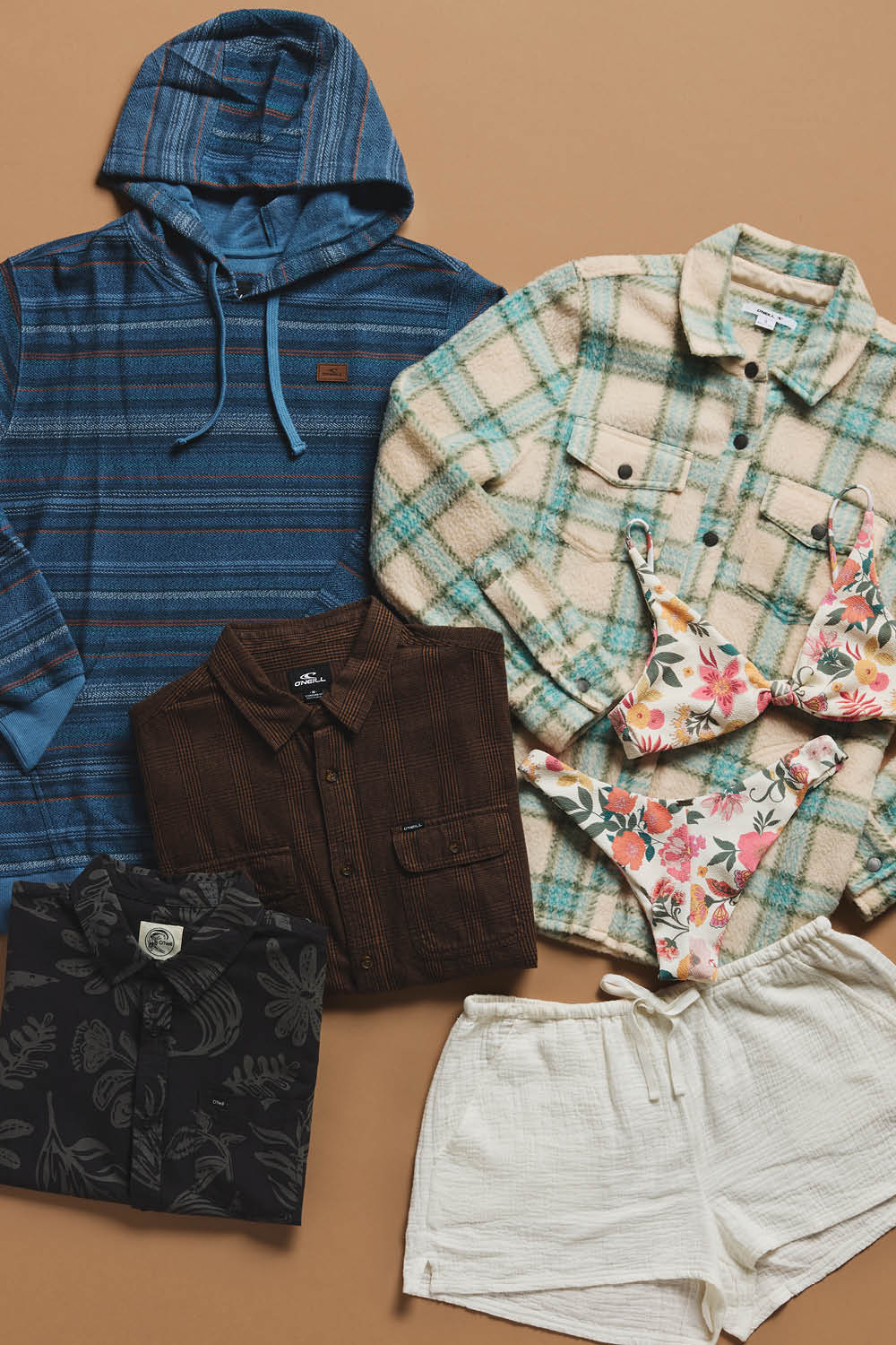 Collection of clothing items including a blue hoodie, plaid shirt, floral shirt, brown jacket, and white shorts on a brown background.