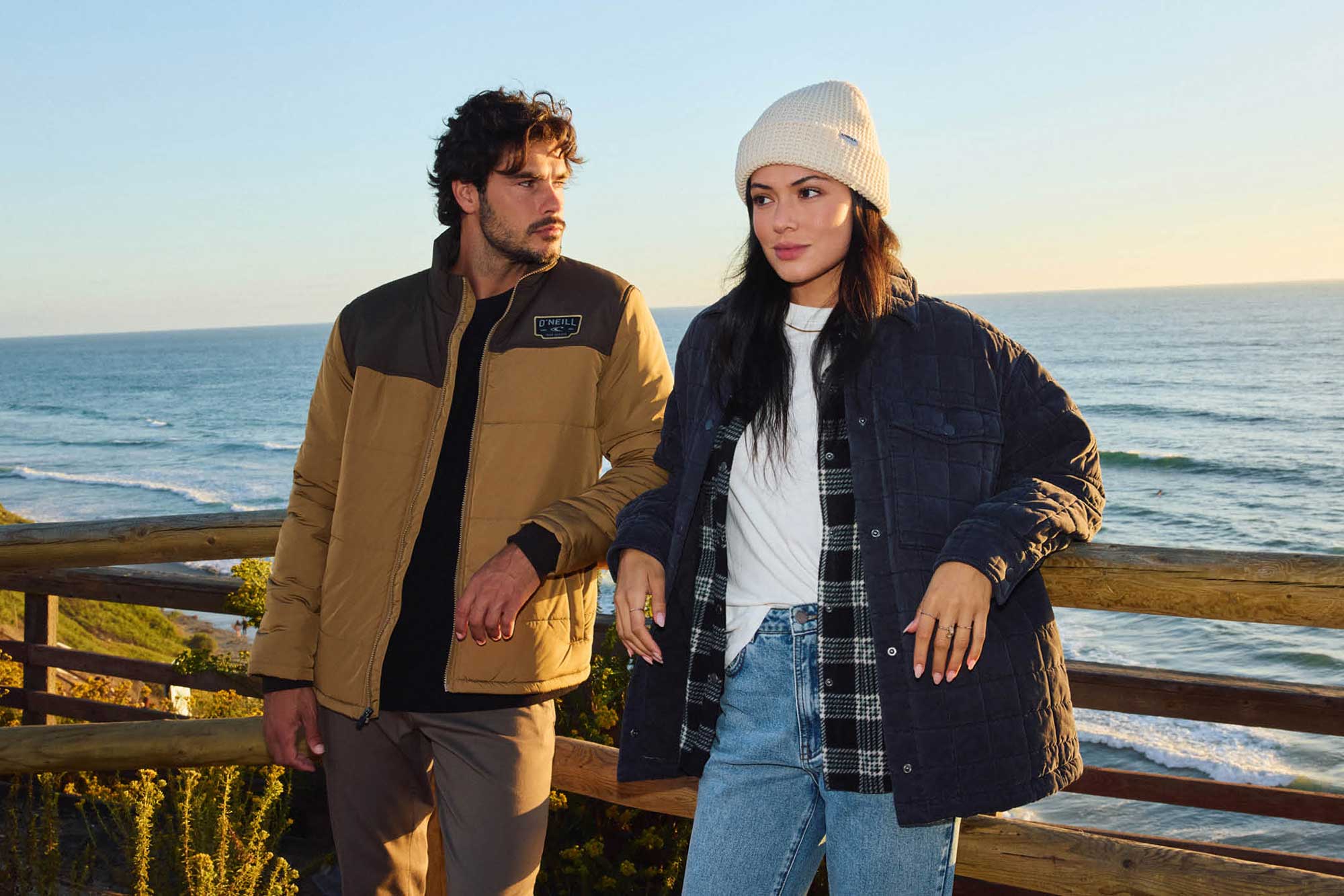 Two people standing on a wooden deck by the ocean