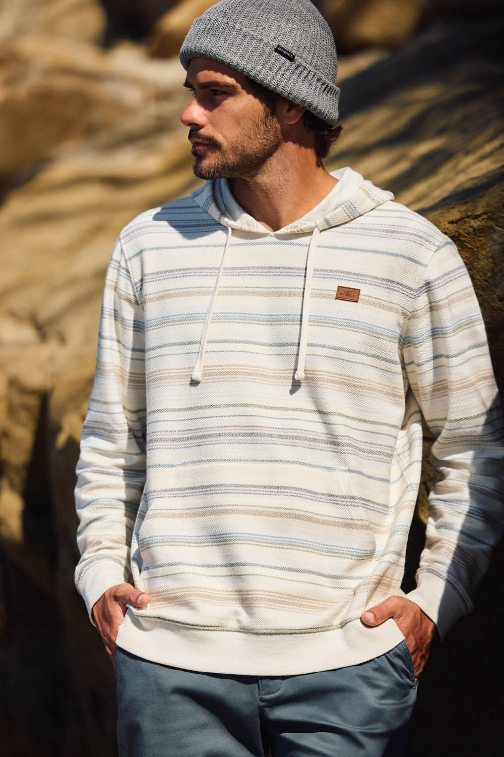 Man wearing a striped hoodie and beanie standing against a rocky background