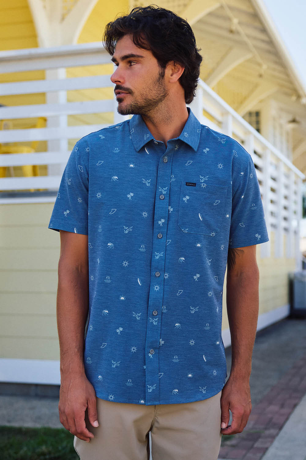 Man wearing a blue patterned shirt standing in front of a yellow building.