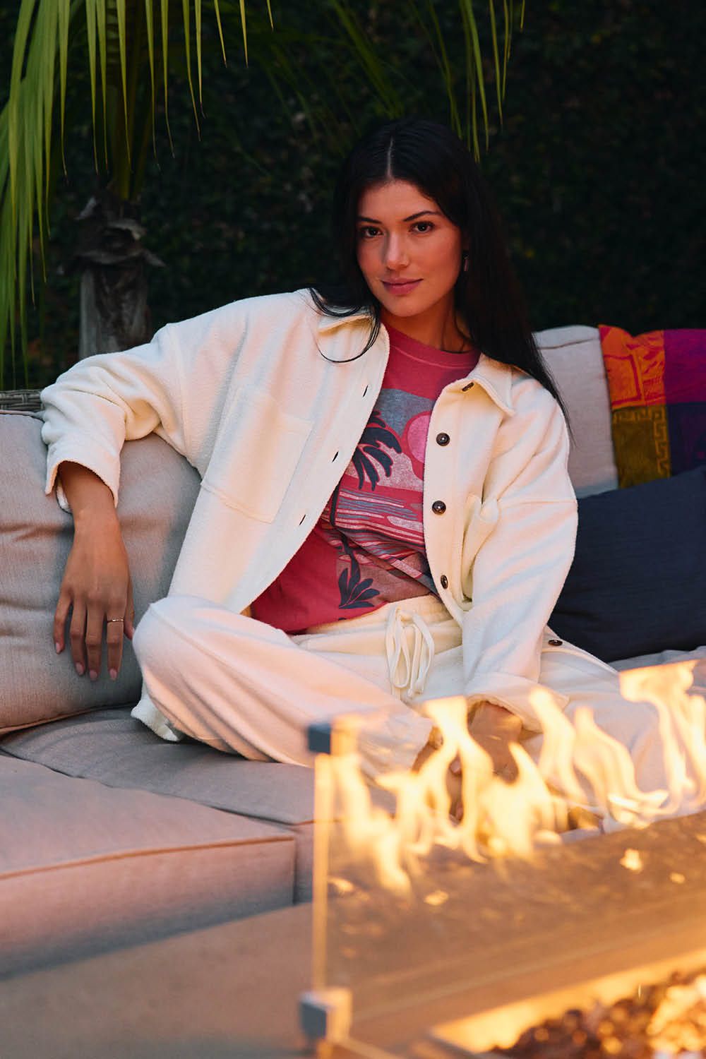 Woman sitting on a couch by a fire pit with a colorful pillow