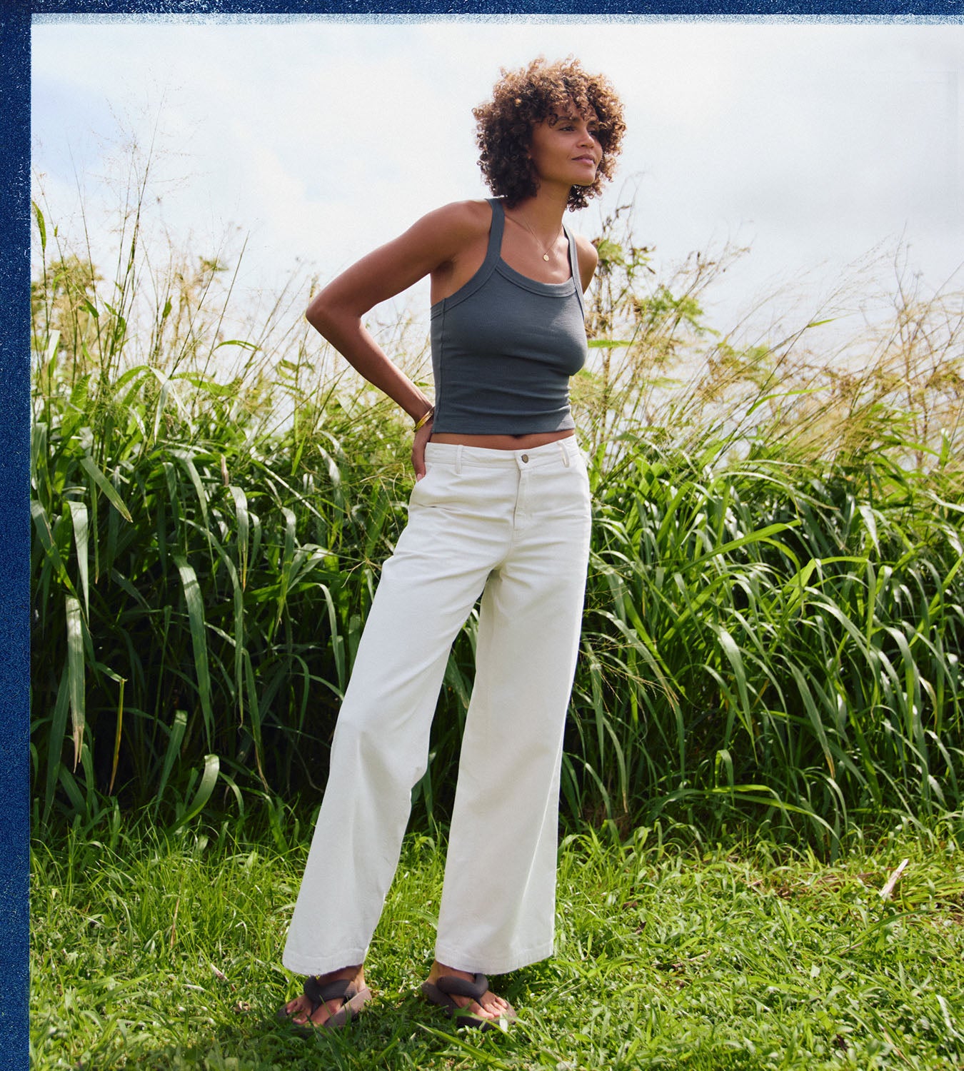 Woman standing in a field wearing a tank top and pants.
