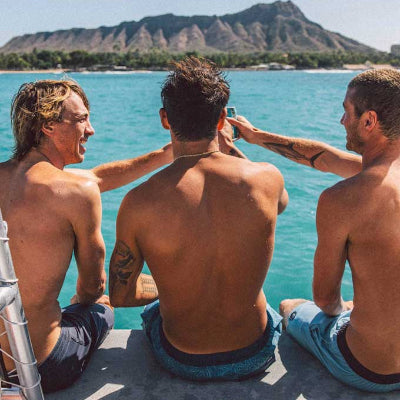 Three men sitting by the ocean with a mountain in the background