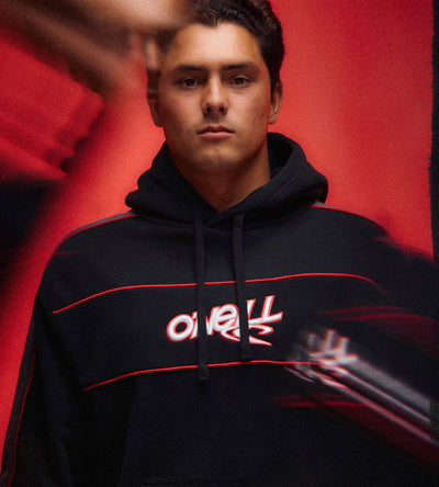 A man wearing a black hoodie with red stripes and a white/red 'overland' logo on the chest, posed against a textured red background.