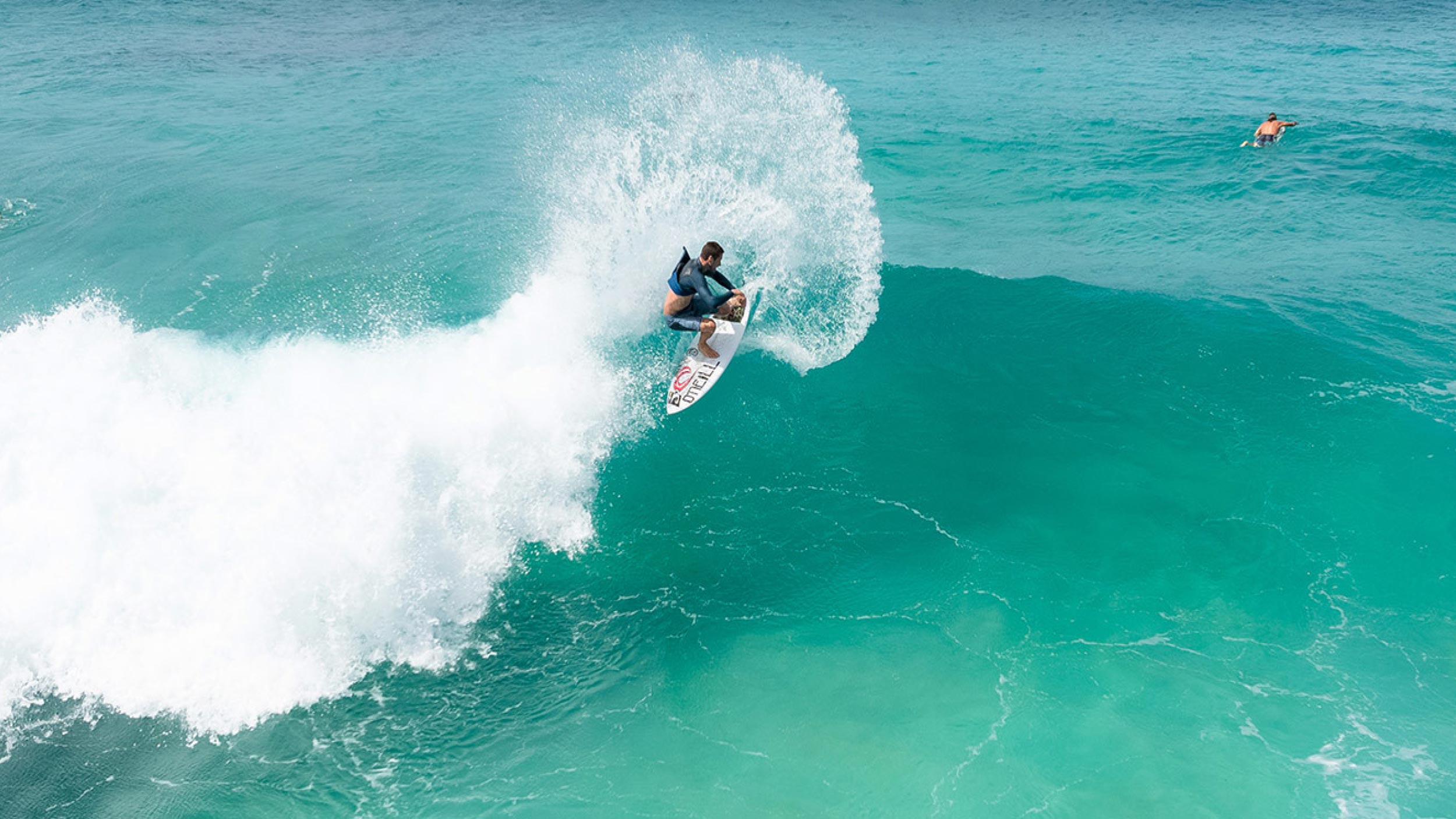 Person surfing a large wave in clear blue water